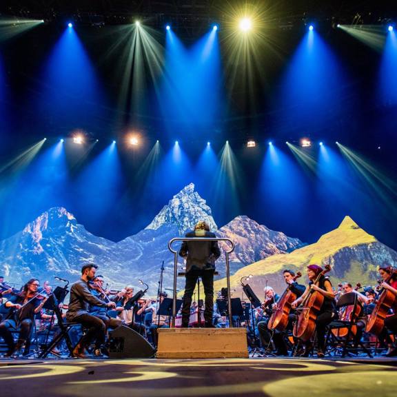 An orchestra perform on stage, with a snowy mountain backdrop.