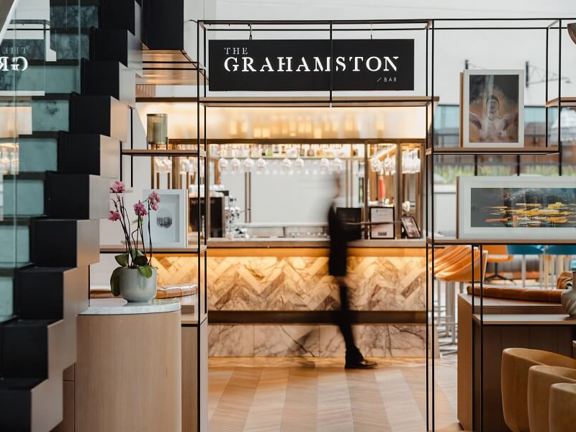 Black mental doorframe with sign above that read The Grahamston Bar. View through doorway to marble,, glass and brass bar. 