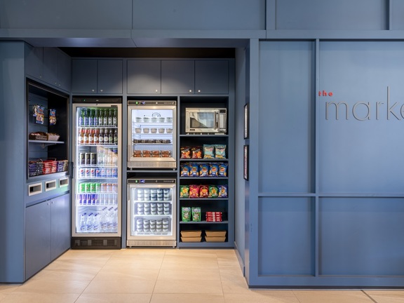 Self service buffet area with fridges and shelves filled with drinks and food for self-preparation. 