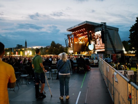 An attendee using crutches watches the TRNSMT main stage from the accessible area with a woman