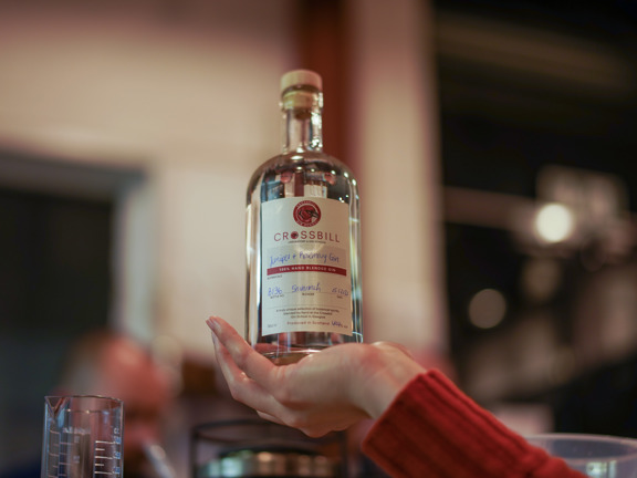 A bottle of Crossbill Gin being held up on the palm of a hand