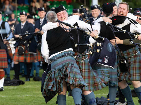 A group of pipers wearing kilts hug and celebrate their win at the World Pipe Band Championships.