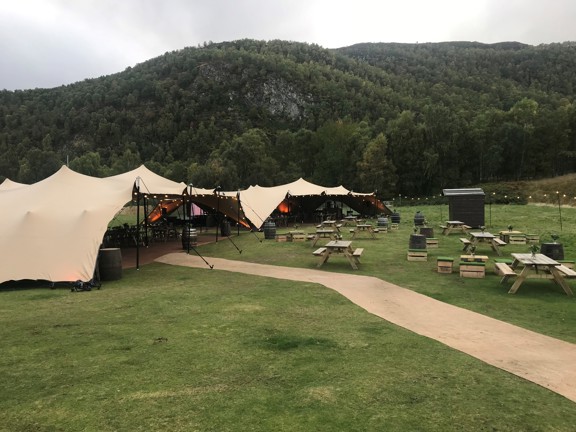 Large glamping stretch tent set up in front of a hill picnic benches in front. 