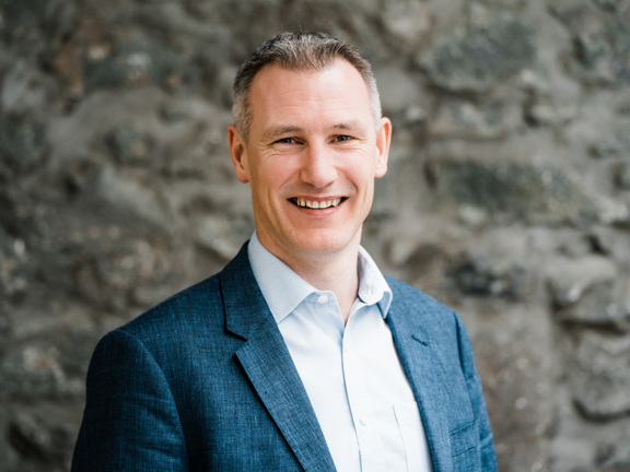 Man wearing shirt and suit jacket smiling and looking at the camera.