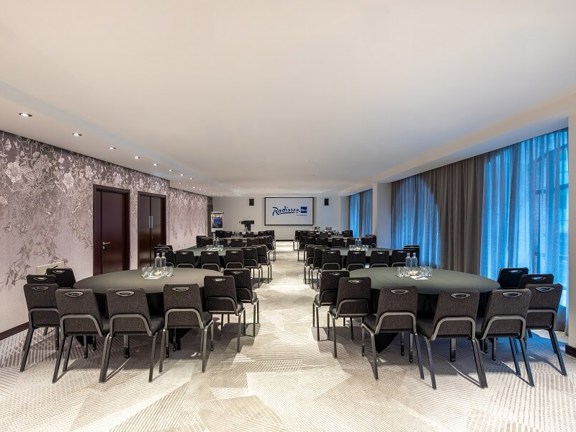 Bright and light hotel meeting room at Radisson Blu with dark grey banquet chairs set up cabaret style and floor to ceiling windows.