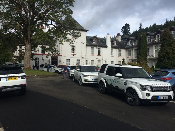 Large period white building set amongst trees is the backdrop for six white Discovery Land Rovers