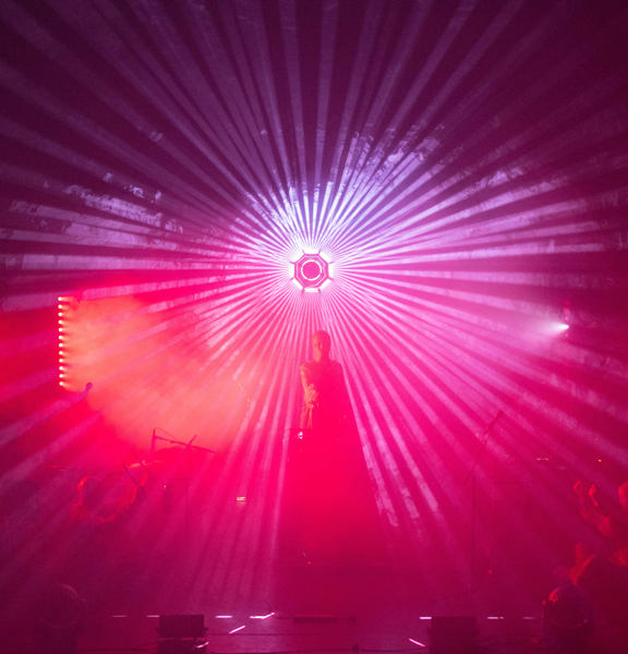 Musician stands in front of pink and purple light 