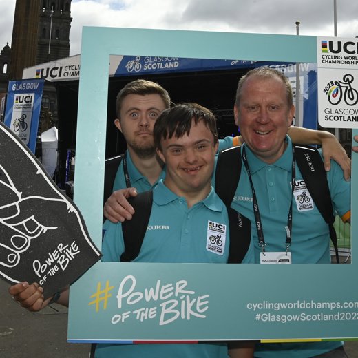 Three volunteers pose wearing blue shirts pose within a social media frame prop