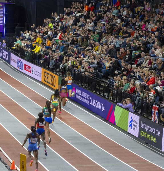 Busy seated crowd watch athletes run on the track.