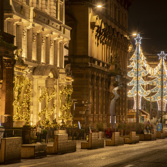 Night-time view of town house decorated with illuminated garlands spiralling around columns and George Square with 5 large Christmas-tree shaped illuminations.