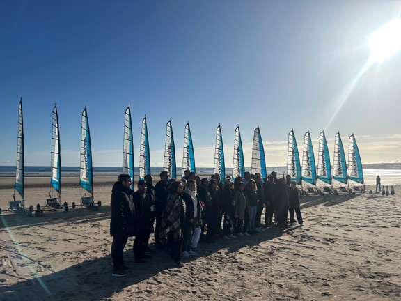 A group of people get ready to try sand yachting in the winter sun on a beach. 