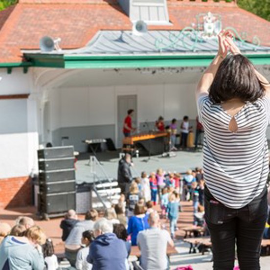 A woman in a striped top standing up and applauding at Kelvingrove Bandstand.