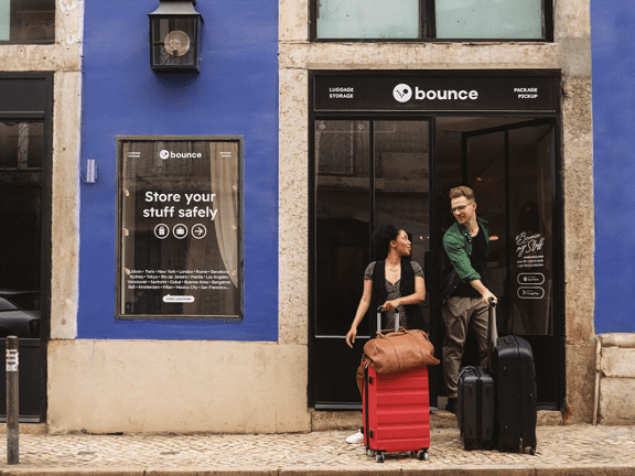 Two people with luggage outside a Bounce luggage storage shop