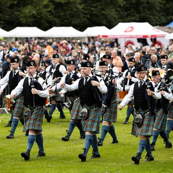 Pipers march across Glasgow Green with green kilts on as a large crowd gathers to watch