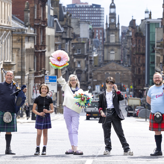 5 people standing on top of a hill in the city centre, some with kilts and bag pipes