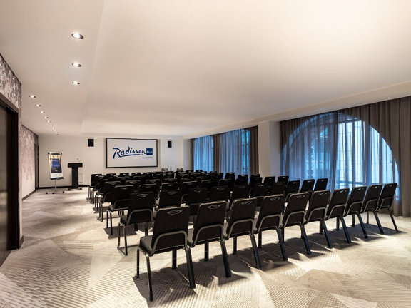 Bright and light hotel meeting room at Radisson Blu with dark grey banquet chairs set up theatre style and floor to ceiling windows.