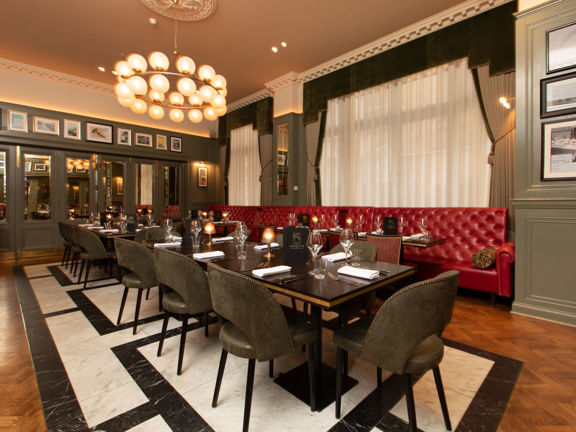 Restaurant interior, long table down the middle of a prvate dinign room. One side have a deep red leather banquette seating and the other dark green velvet chairs. 