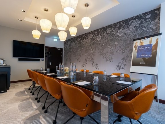 Hotel meeting room at Radisson Blu set up boardroom style with a large glass and metal table and tan leather chairs. 