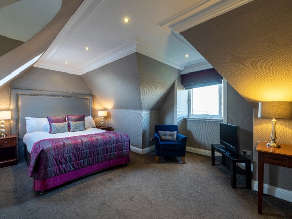 Cosy hotel bedroom in the eves of the attic - dark grey walls and large bed with red and grey tartan cover